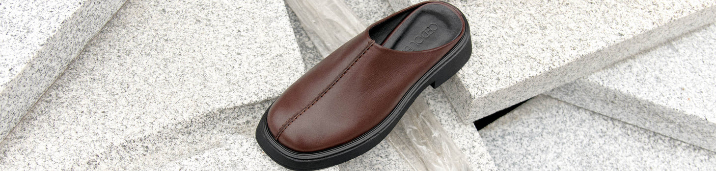 Schwarzes Schuhpaar aus Leder steht auf einem Lederhocker vor einem Vorhang