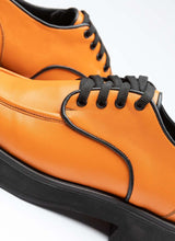 Lade das Bild in den Galerie-Viewer, Detailansicht eines orangefarbenen Unisex-Lederschuhs mit Schnürsenkeln in schwarz, farblich angesetzter Paspel in schwarz und einer dezenten, schwarzen Plateausohle