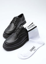 Lade das Bild in den Galerie-Viewer, Ein Paar Lederschuhe in schwarz sowie eine weiße Tennissocke mit CEDOUBLÉ Logo. Die Schuhform ist eine Mischung aus Karree und rund. Die aufgeworfene Wulstnaht auf dem vorderen Schaftteil verschlankt optisch die modische chunky Form.