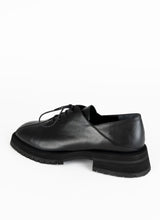 Lade das Bild in den Galerie-Viewer, Produktfoto eines burschikosen Unisex-Schnürschuhs aus Leder mit Oxford-Schnürung und ausgeprägter Laufsohle in schwarz. Eine asymmetrische Naht ziert die Schuhfront