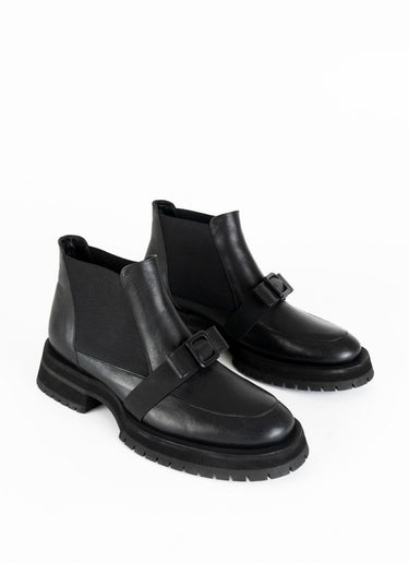 Ein Paar schwarze Chelseaboots aus Leder mit weitflächigem Elastikeinsatz und dekorativer Schnalle in Schleifenoptik. Dieses Schleifendetail schmiegt sich über den Spann.