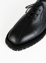 Lade das Bild in den Galerie-Viewer, Detailfoto eines burschikosen Leder Derbys mit Oxford-Schnürung und ausgeprägter Laufsohle in schwarz. Eine asymmetrische Naht ziert die Schuhfront