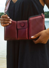 Lade das Bild in den Galerie-Viewer, Das Foto zeigt den Oberkörper eines Models mit einem weiten, schwarzen Kleid. Zu sehen sind zwei gepflegte Hände, die eine rote Crossbody Bag mit drei Abteilen umfassen. Die rote Tasche hängt locker am Körper und schmiegt sich den Körperkonturen an. Sie ist von der Marke Cedoublé und wurde aus hochwertigem Lammleder gefertigt.