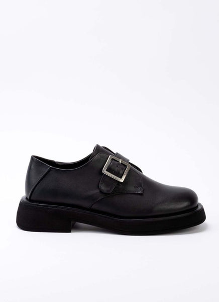 Seitliche Ansicht eines klassisch-coolen Unisex-Schuhs aus zeitlosem, schwarzem Leder mit Riemen und Schnalle. Auch die Laufsohle ist schwarz. Die Schuhspitze ist eine Mischung aus Karree und rund.