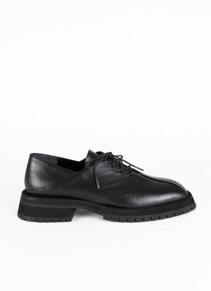 Produktfoto eines burschikosen Leder Derbys mit Oxford-Schnürung und ausgeprägter Laufsohle in schwarz. Eine asymmetrische Naht ziert die Schuhfront