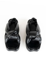 Load image into Gallery viewer, Produktbild einer weich gepolsterten Sandale aus schwarzem Leder mit exzentrischem Knotdendetail, welches den Fuß umhüllt. Ein weicher, geraffter Lederriemen in schwarz fixiert die Ferse. Die Deck- und Laufsohle sind mit schwarzem Leder bezogen
