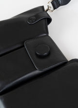 Load image into Gallery viewer, Detailfoto einer schwarzen Crossbody-Bag aus weich gepolstertem Glattleder mit drei voneinander abgetrennten Fächern und einem farblich passenden, breiten Gurt aus Leder mit Karabinerhaken
