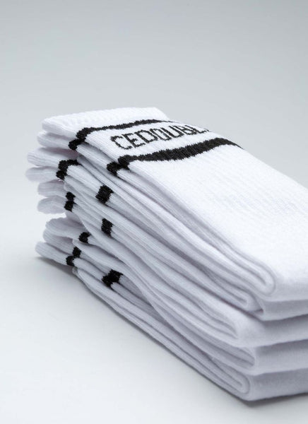 Aufeinander gestapelte Tennissocken des Labels Cedoublé in weiß-schwarz mit Logo. Es handelt sich um ein Produktbild. Auf dem Foto gut ersichtlich ist die Qualität aus Bio-Baumwolle. Die Strümpfe sind unisex tragbar.