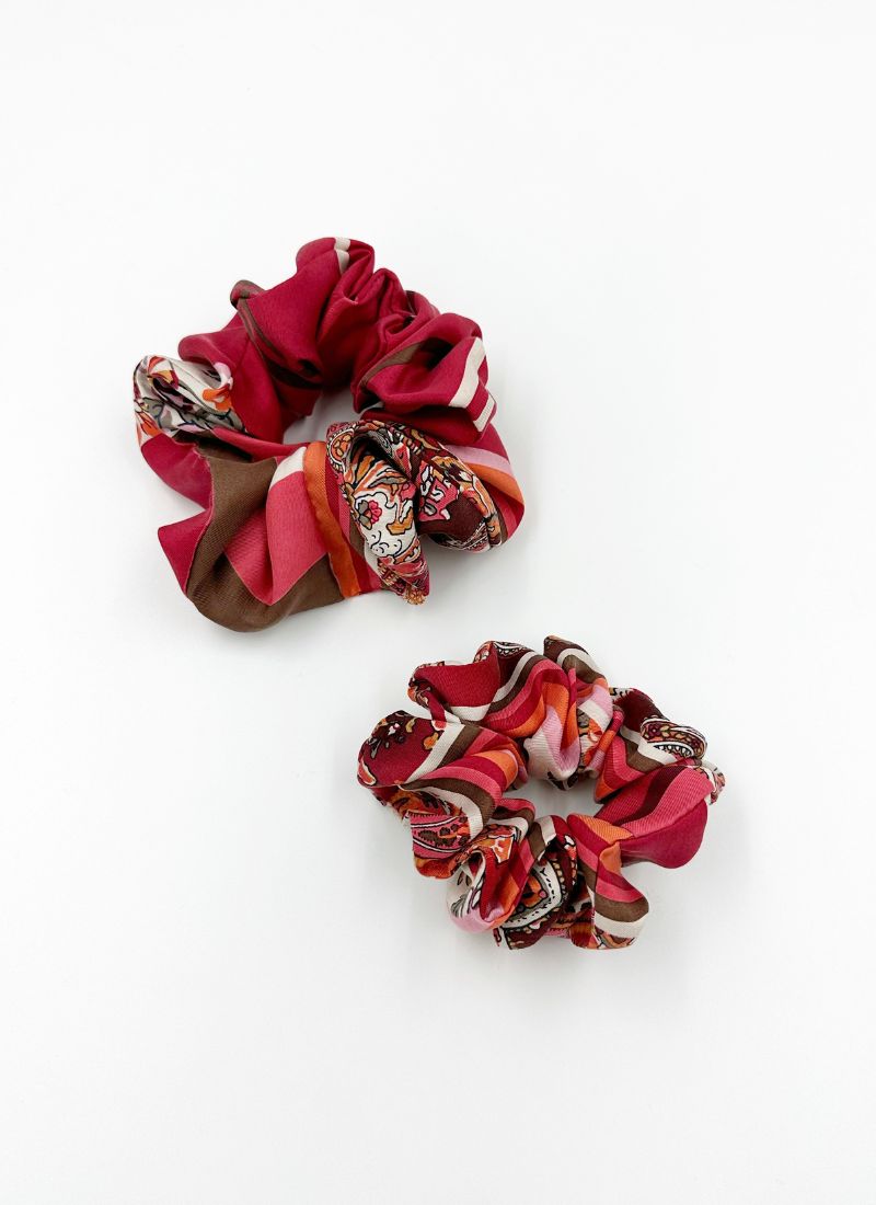 Zwei Scrunchies aus reiner Seide in verschiedenen Rottönen und Mustern. Unter anderem sieht man Partien, die gestreift oder im Paisely-Design gehalten sind.